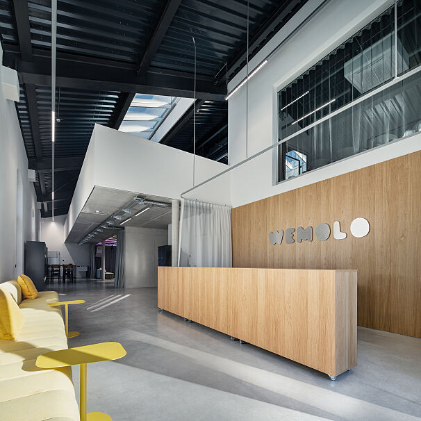 Empfangsbereich im neuen Wemolo-Headquarter im Isarwinkel: Die historische Triebwagenhalle verbindet offene Raumstrukturen mit modernen Arbeitsflächen für Austausch und Zusammenarbeit.