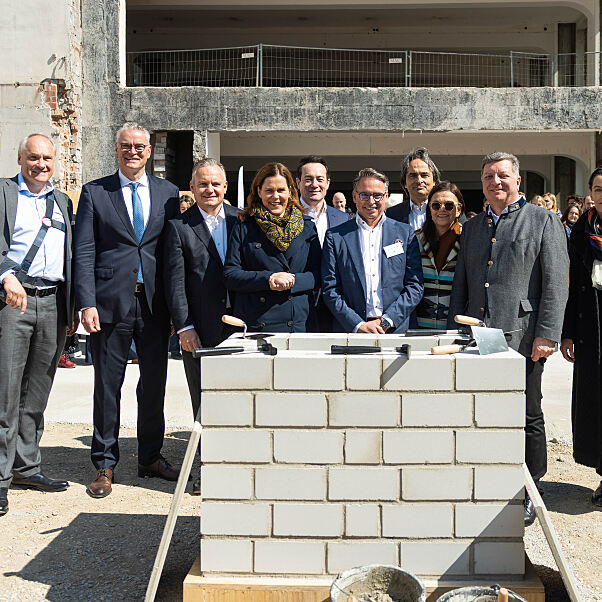 Personen auf dem Foto von links nach rechts: Dr. Matthias Cord; Dr. Constantin H. Alsheimer, Vorstandsvorsitzender der THÜGA; Dr. Christian Scharpf, Referent für Arbeit und Wirtschaft; Verena Dietl, Dritte Bürgermeisterin von München; Christian Lealahabumrung, Grüner und Gesellschafter der Rock Capital Group; Andreas Wißmeier, Geschäftsführer der Rock Capital Group; Peter G. Neumann, Gründer und Gesellschaftler der Rock Capital Group; Stadtbaurätin Prof. Dr. (Univ. Florenz) Elisabeth Merk; Christian Bernreiter, Staatsminister für Wohnen, Bau und Verkehr; Rita Ahlers, Partnerin und Architektin bei Hilmer Satller Architekten.