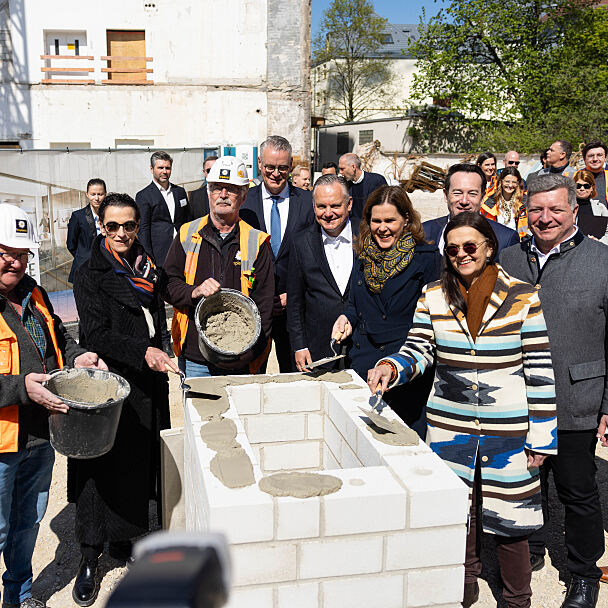 Personen auf dem Bild von links nach rechts: Implenia, Rita Ahlers, Partnerin und Architektin bei Hilmer Satller Architekten; Implenia; Constantin H. Alsheimer, Vorstandsvorsitzender der THÜGA; Dr. Christian Scharpf, Referent für Arbeit und Wirtschaft; Verena Dietl, Dritte Bürgermeisterin von München; Stadtbaurätin Prof. Dr. (Univ. Florenz) Elisabeth Merk; Christian Lealahabumrung, Grüner und Gesellschafter der Rock Capital Group; Christian Bernreiter, Staatsminister für Wohnen, Bau und Verkehr; Andreas Wißmeier, Geschäftsführer der Rock Capital Group.  