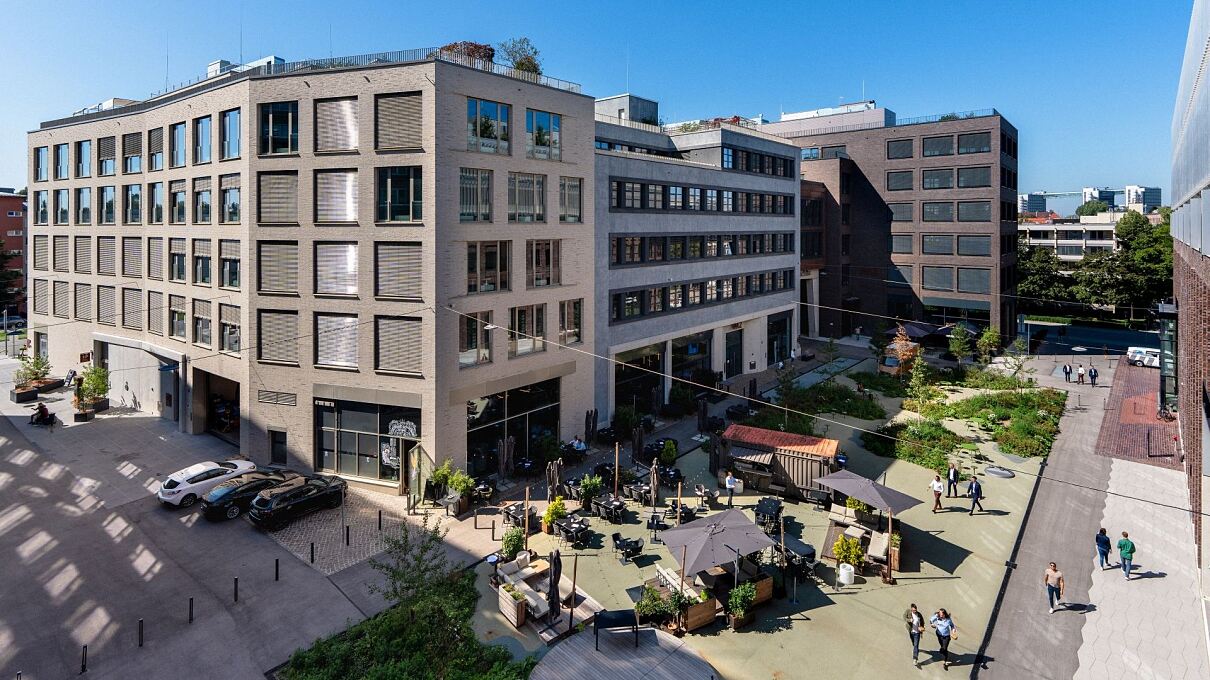 Mixed Use im Münchner Osten: Rund um den zentralen Quartiersplatz der Macherei München liegen sechs Gebäude mit mehr als 75.000 Quadratmetern Mietfläche für Büro, Gastronomie, Handel, Hotel und Fitness. Seit Juli 2026 ergänzt eine Kita den Nutzungsmix.