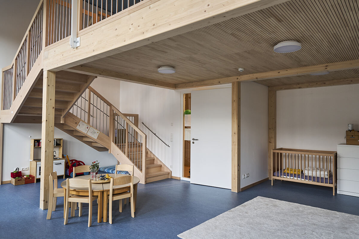 Holzeinbauten mit Treppe und Galerie nutzen die große Raumhöhe eines Gruppenraums. Auf mehreren Ebenen entstehen Spiel-, Bewegungs- und Rückzugsbereiche.