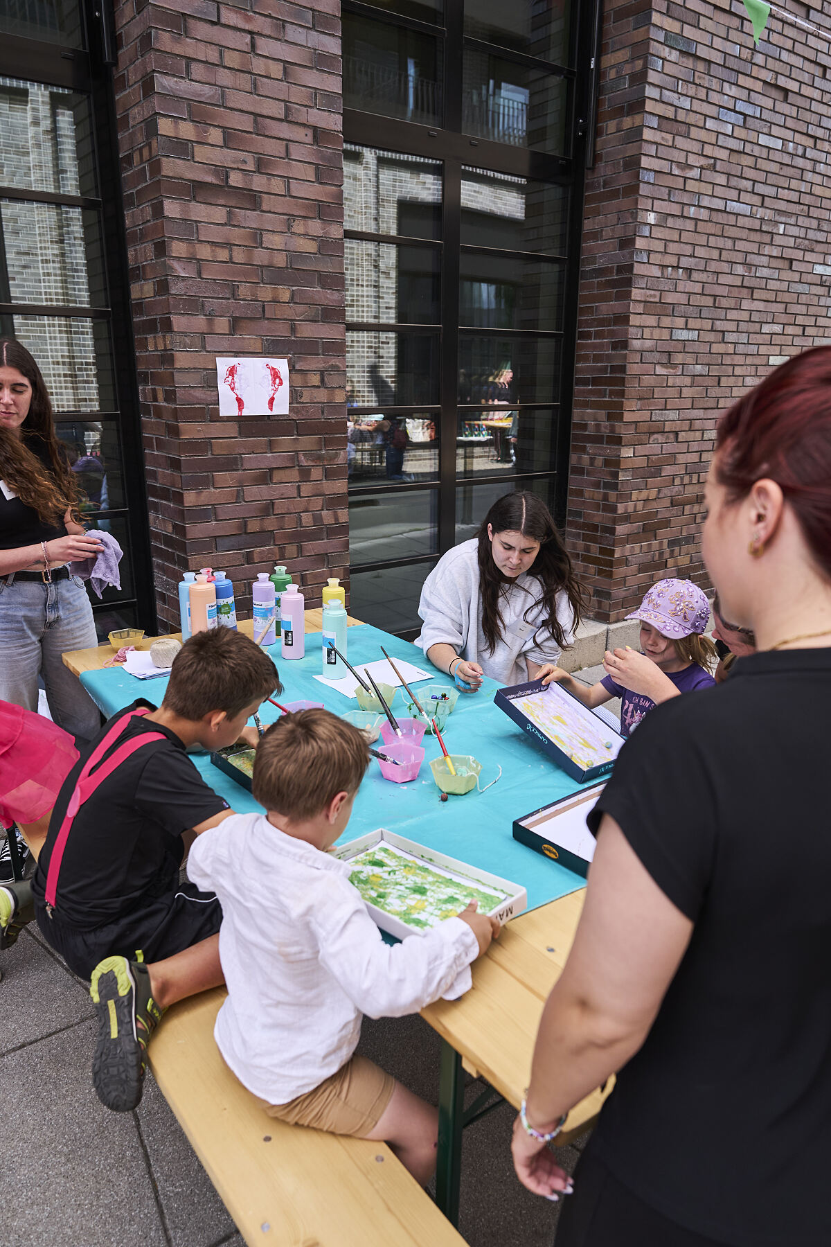 Kinder und Erwachsene gestalten am Basteltisch Bilder mit Farben, Stempeln und Naturmaterialien.