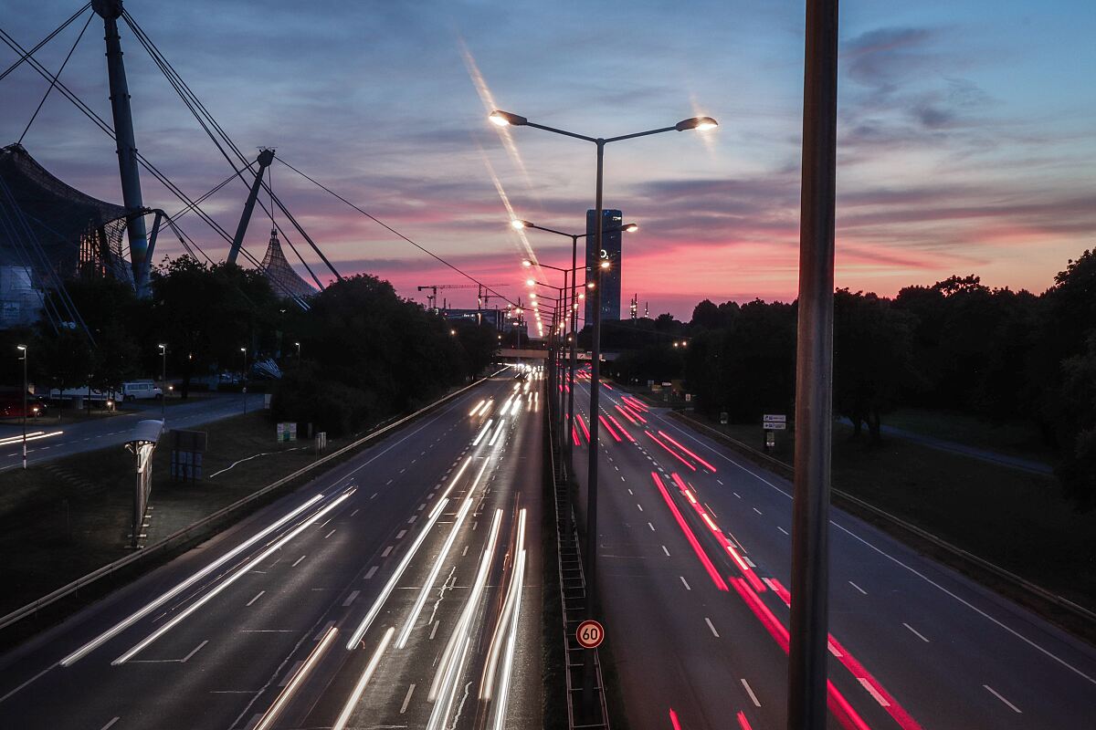 Abendverkehr auf dem Mittleren Ring am Olympiapark in München, Langzeitbelichtung. Der Straßenraum ist knapp, private Parkplätze von Handel und Büro stehen nach Feierabend oft leer.