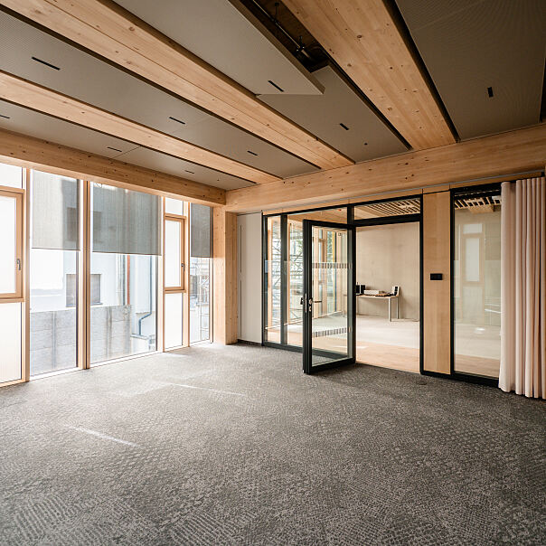 Showroom (gleicher Raum) mit direkter Sicht auf die hölzerne Fensterfassade und das Wechselspiel von Licht und Textur.