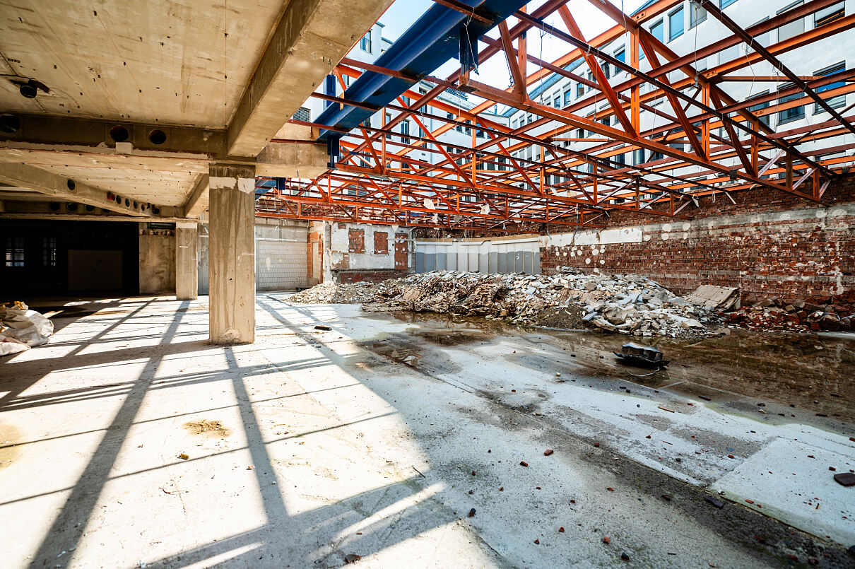 Freigelegte Dachhalle mit Stahlfachwerk: Hier wird deutlich, wie im Bestand gearbeitet wird. Die neue Struktur entsteht, ohne die tragende Substanz vollständig zu ersetzen.